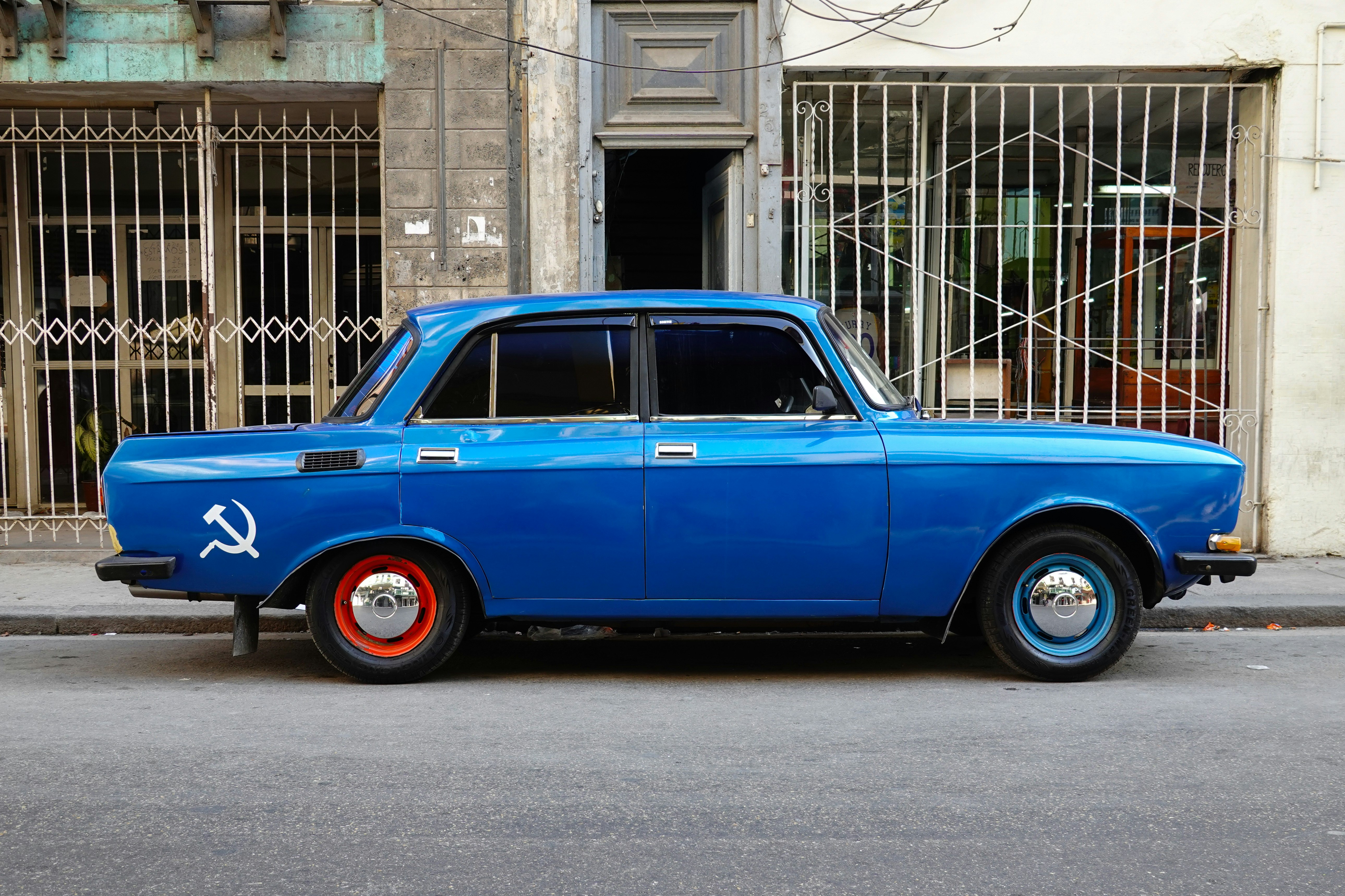 blue sedan parked beside brown concrete building during daytime